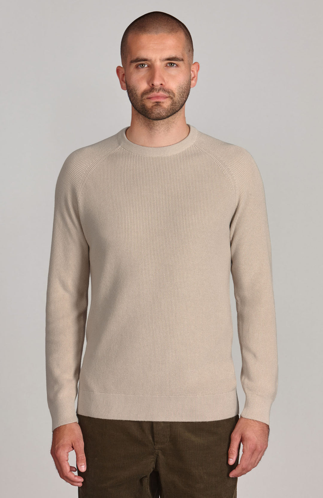 A male model wearing a beige long sleeve crew neck cotton fisherman rib jumper.