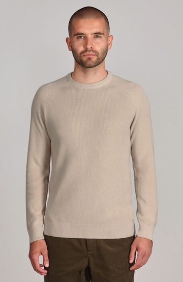 A male model wearing a beige long sleeve crew neck cotton fisherman rib jumper.