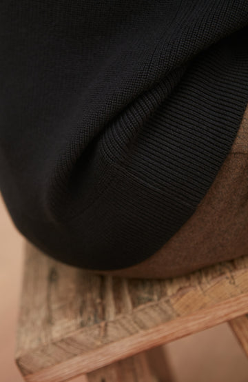 Close-up of a black rib jumper on a woven surface