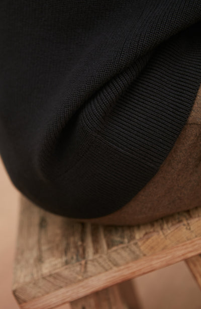 Close-up of a black rib jumper on a woven surface