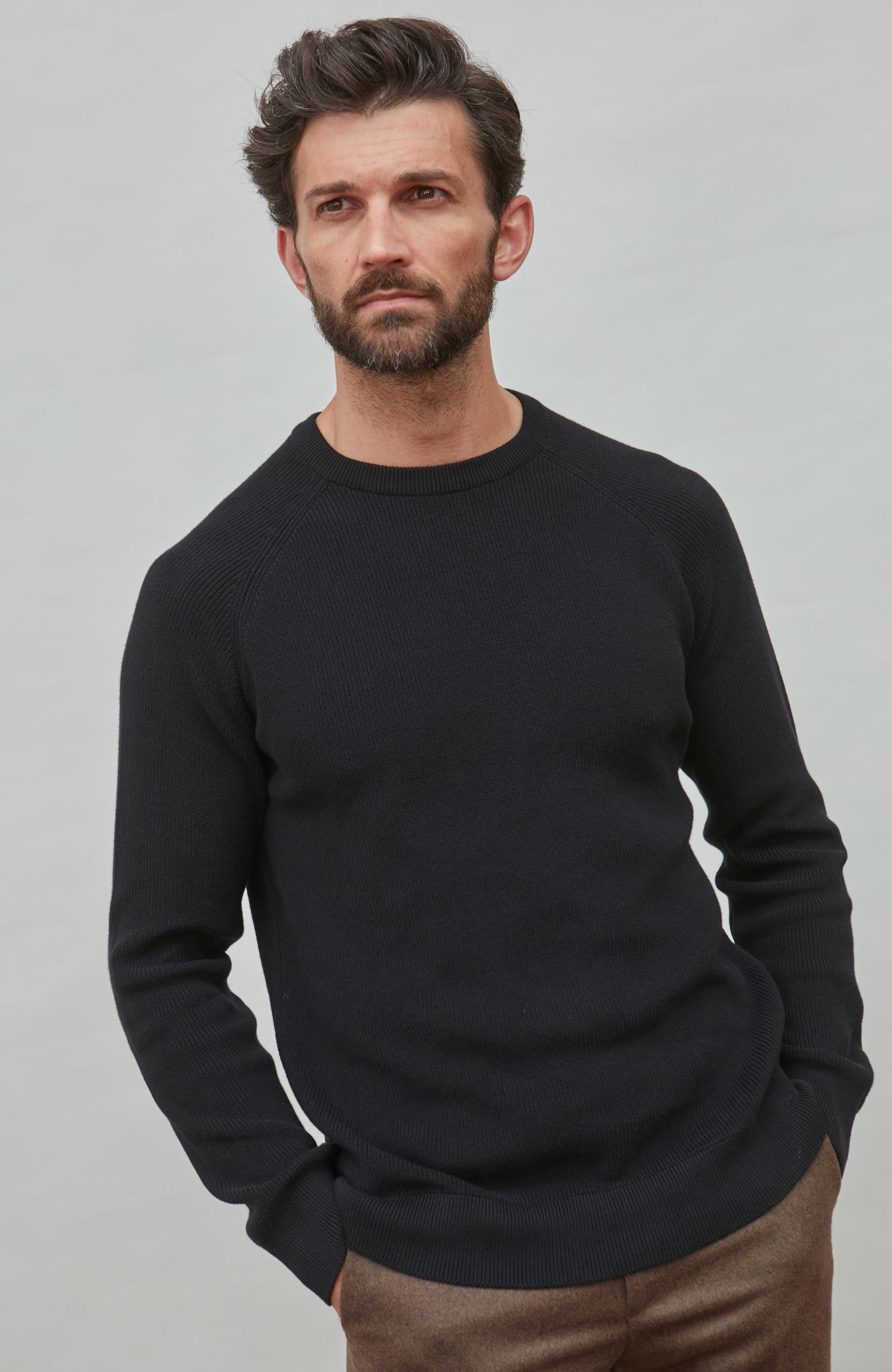 Man wearing a black cotton rib sweater against a gray background
