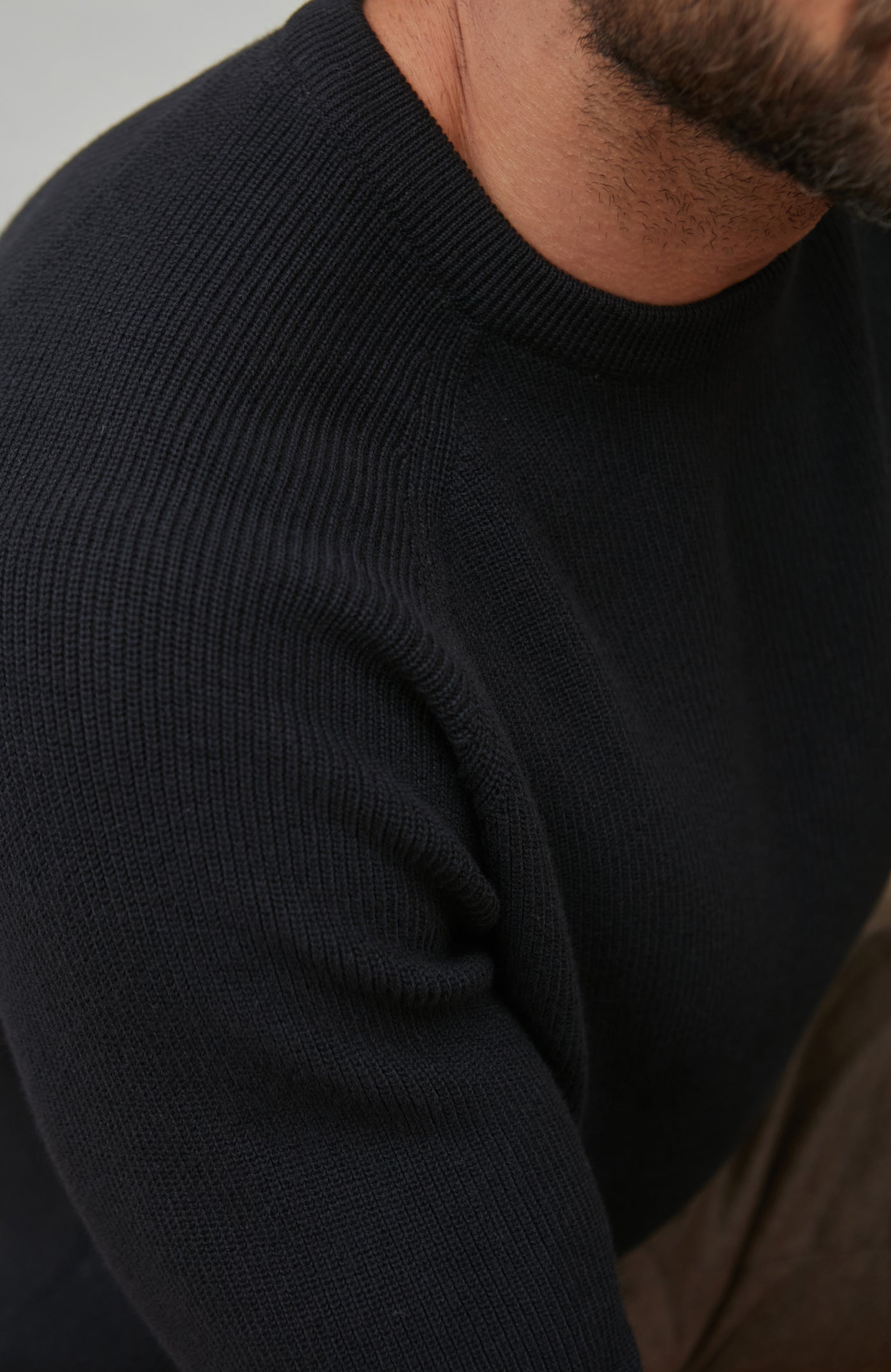 Close-up of a person wearing a black rib sweater with a neutral background