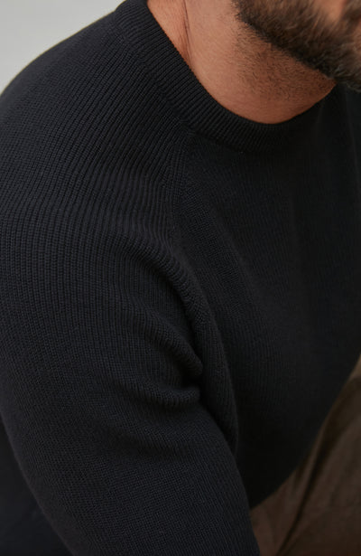 Close-up of a person wearing a black rib sweater with a neutral background