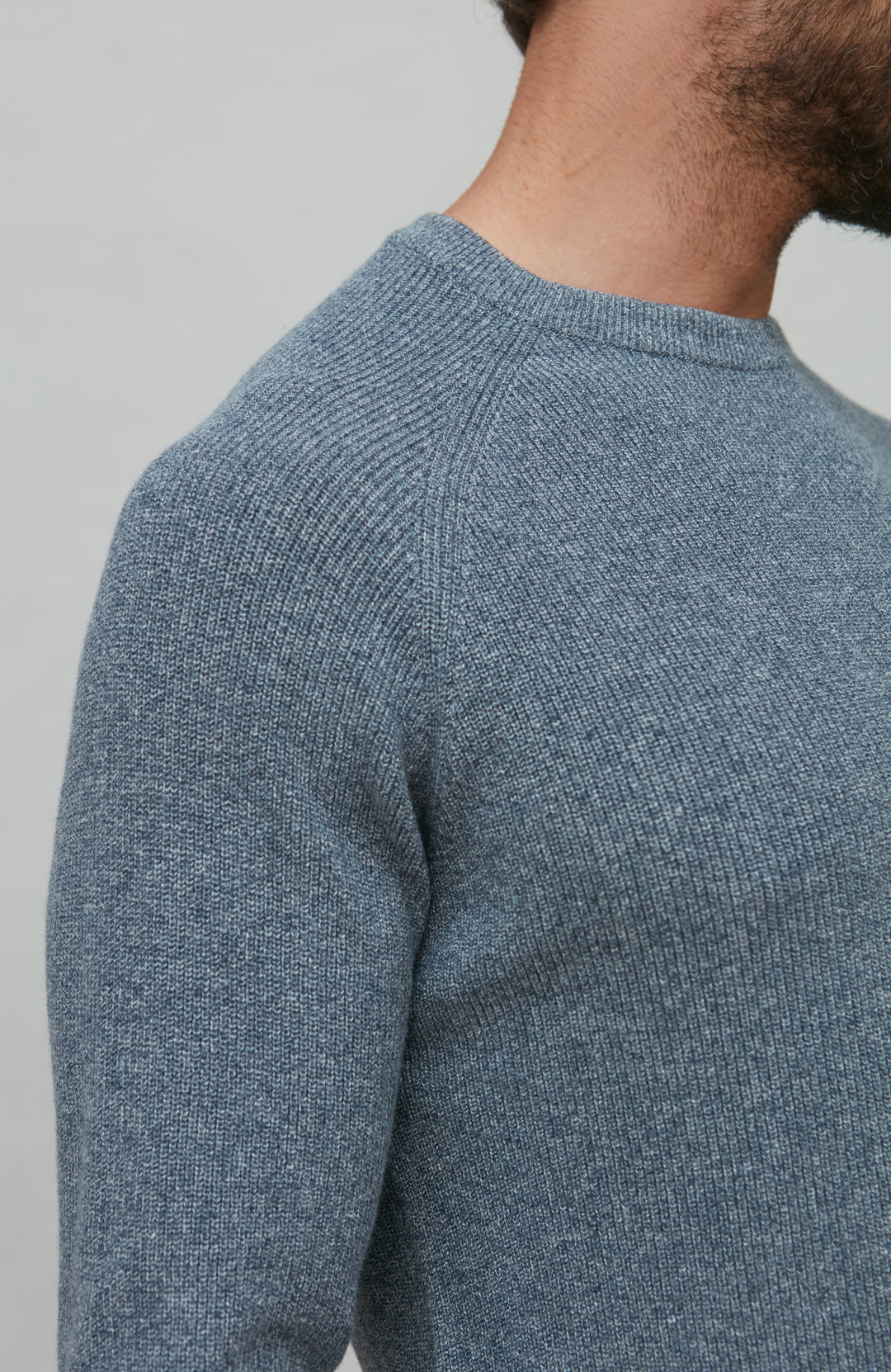 Close-up of a person wearing a blue cotton rib sweater against a gray background