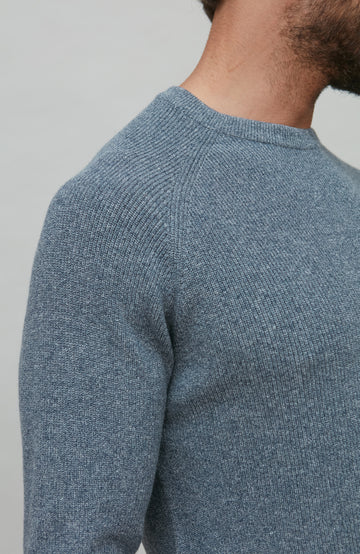 Close-up of a person wearing a blue cotton rib sweater against a gray background
