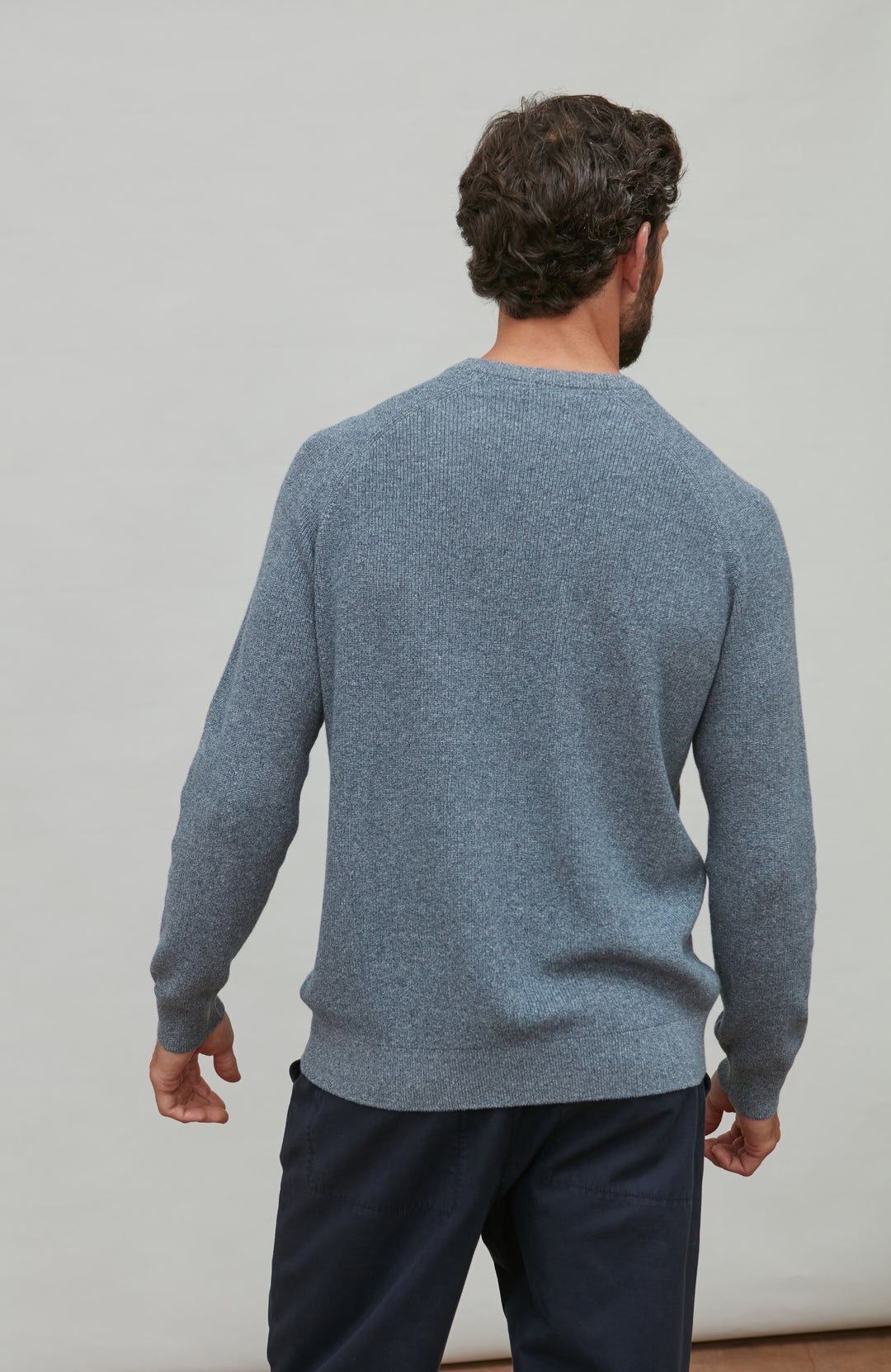 Man wearing a blue cotton rib jumper and dark pants against a plain background