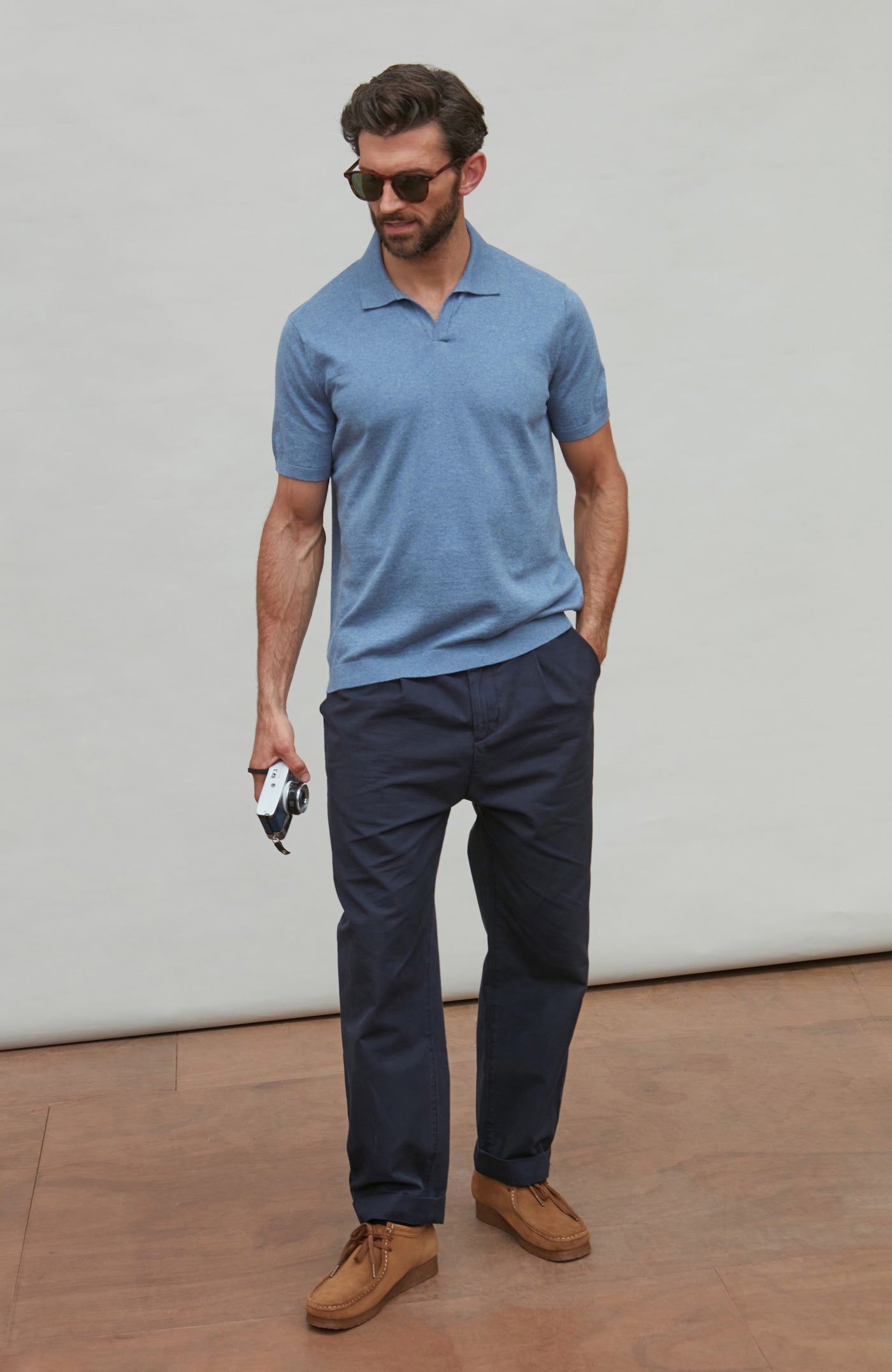 Man wearing a blue polo shirt and navy pants standing against a plain background