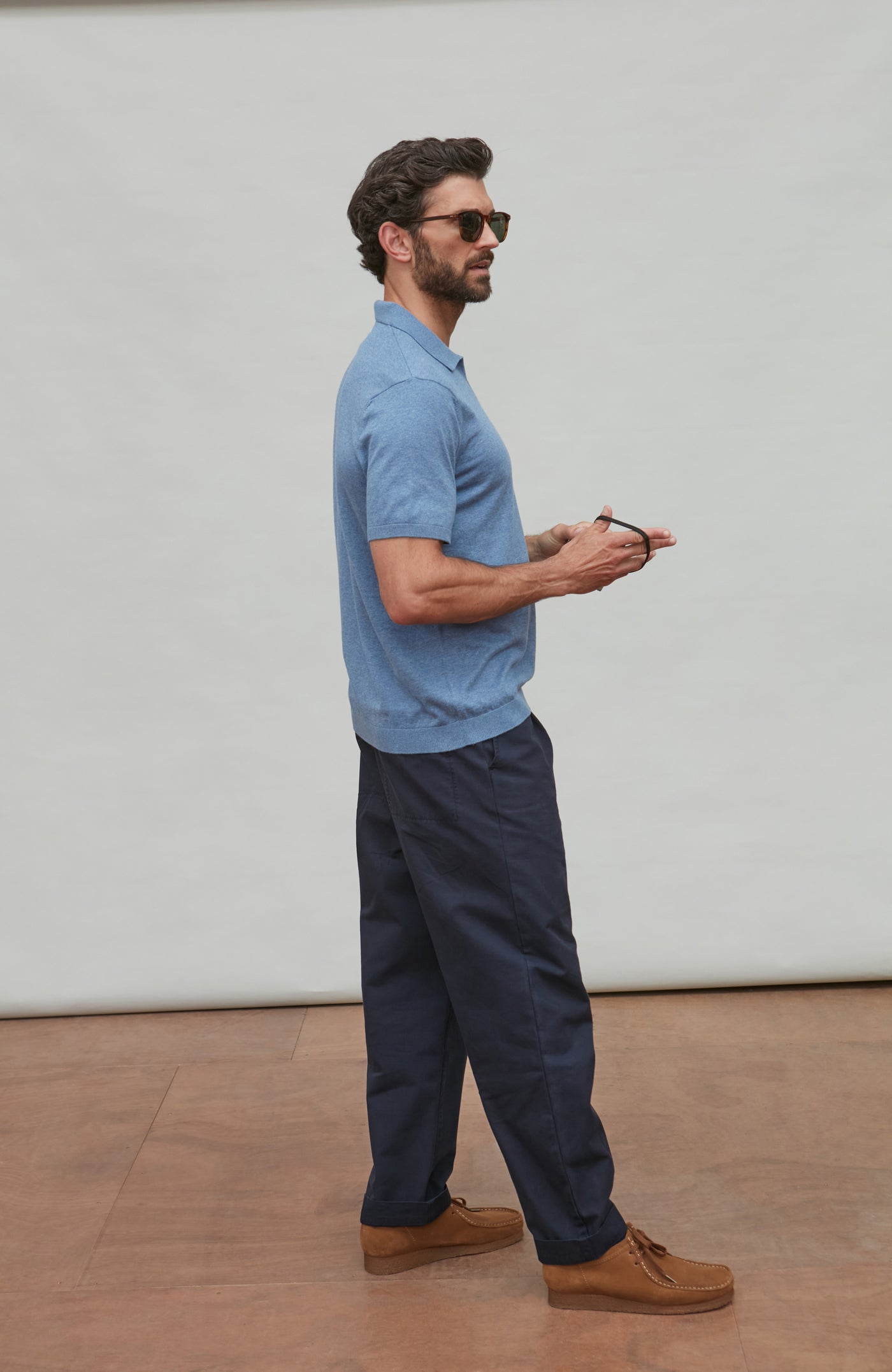 Man wearing a light blue shirt and dark pants standing against a white wall.