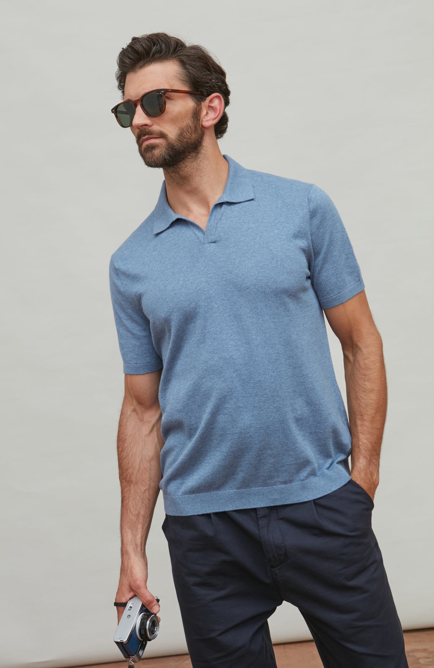 Man wearing a blue polo shirt and dark pants against a plain background