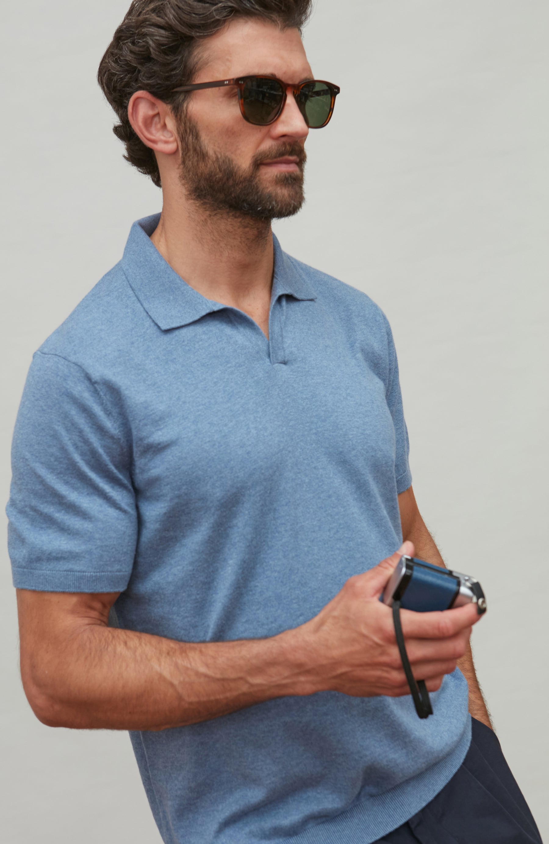 Man wearing a blue polo shirt holding a phone against a gray background