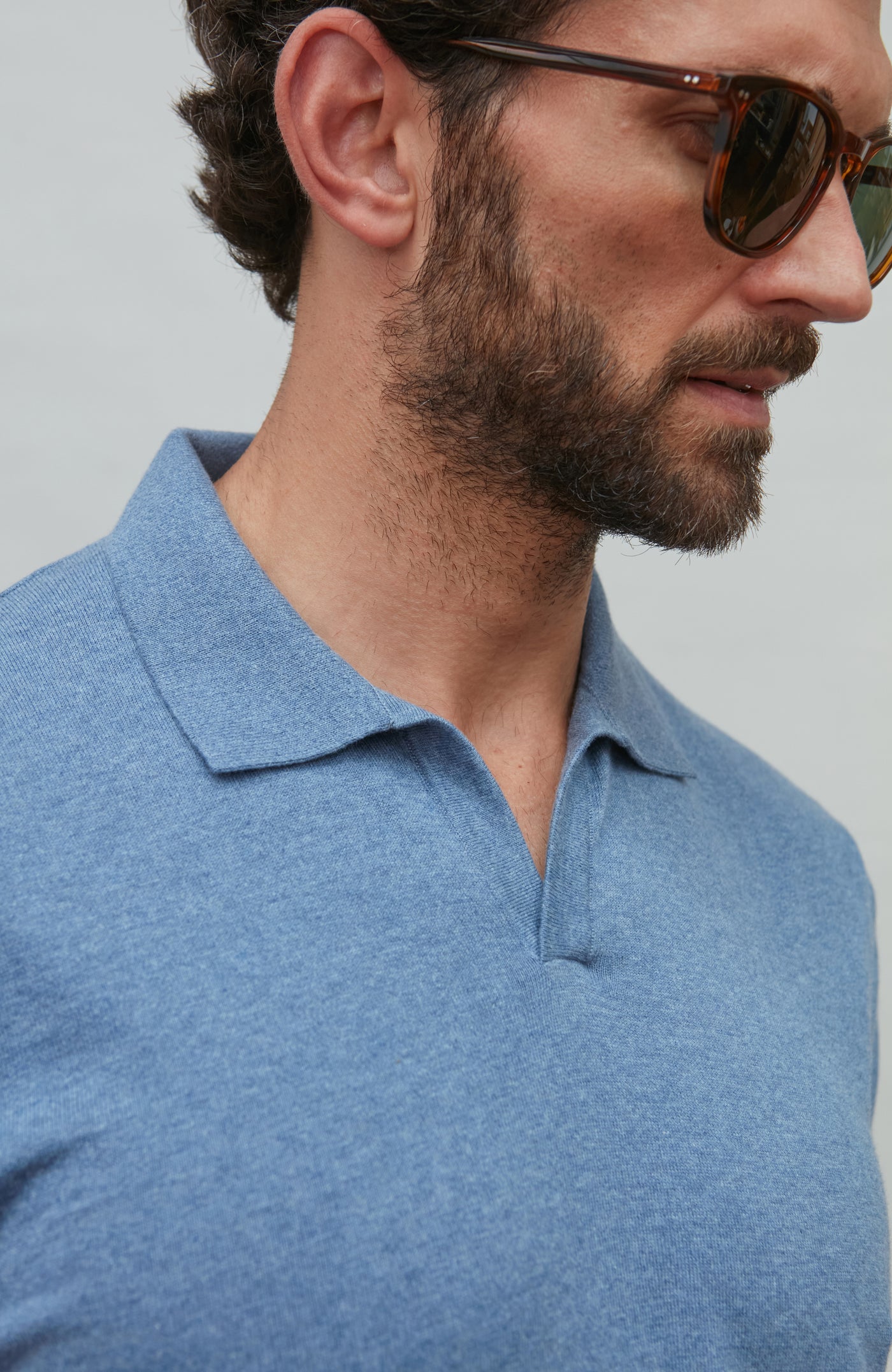Man wearing a blue polo shirt and sunglasses against a gray background