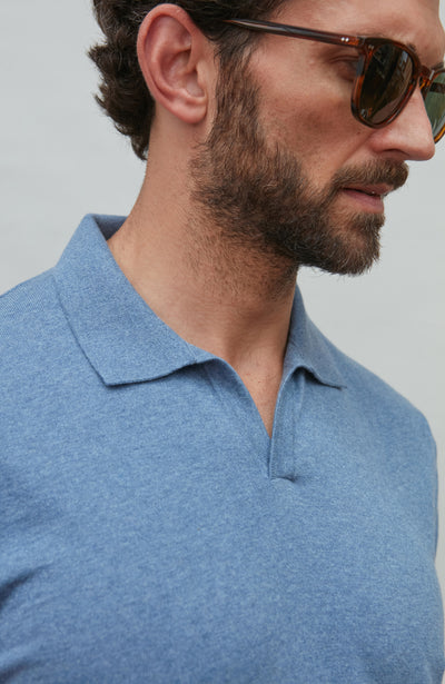 Man wearing a blue polo shirt and sunglasses against a gray background