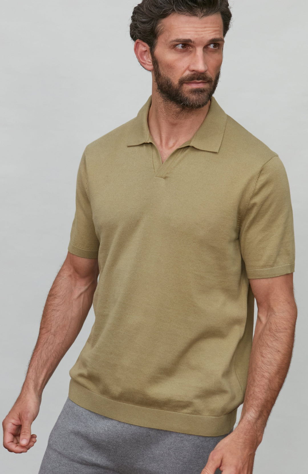 Man wearing a green polo shirt and gray pants against a plain background