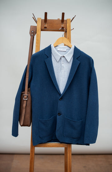 Blue mens blazer by paul james over a white shirt on a wooden hanger with a brown leather bag.