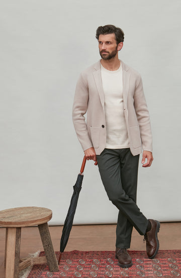 Man in a beige blazer holding an umbrella against a plain background