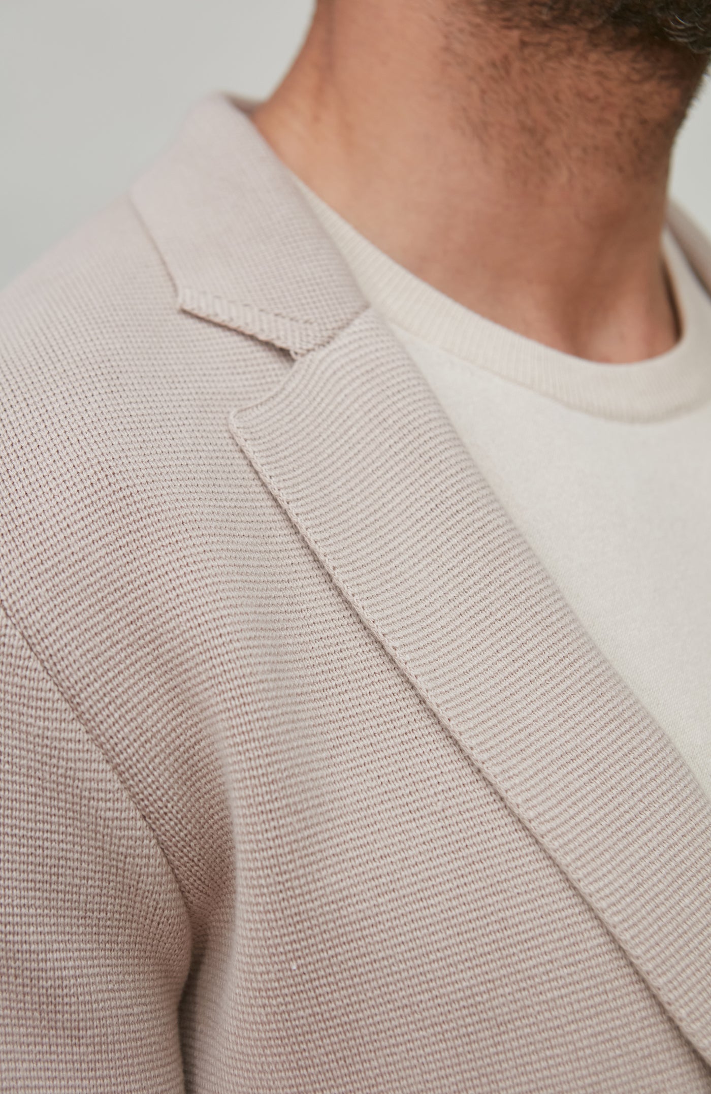 Close-up of a person wearing a light brown textured blazer over a white shirt.