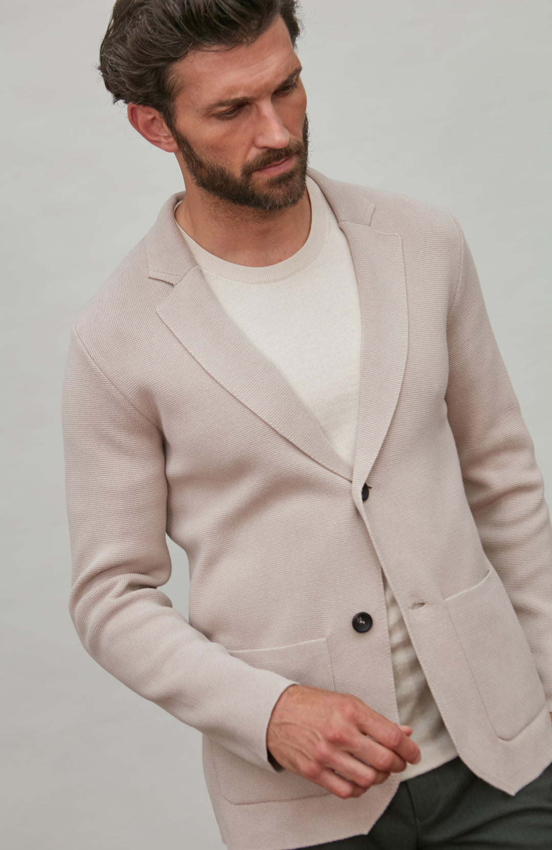 Man wearing a light beige blazer over a white shirt on a plain background