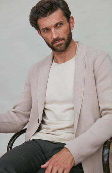 Man wearing a light beige blazer over a white shirt with a neutral background