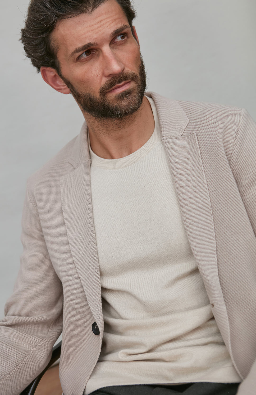 Man wearing a beige blazer over a white shirt against a plain background