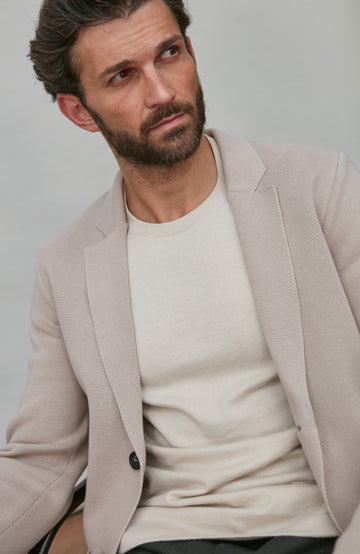 Man wearing a beige blazer over a white shirt against a plain background