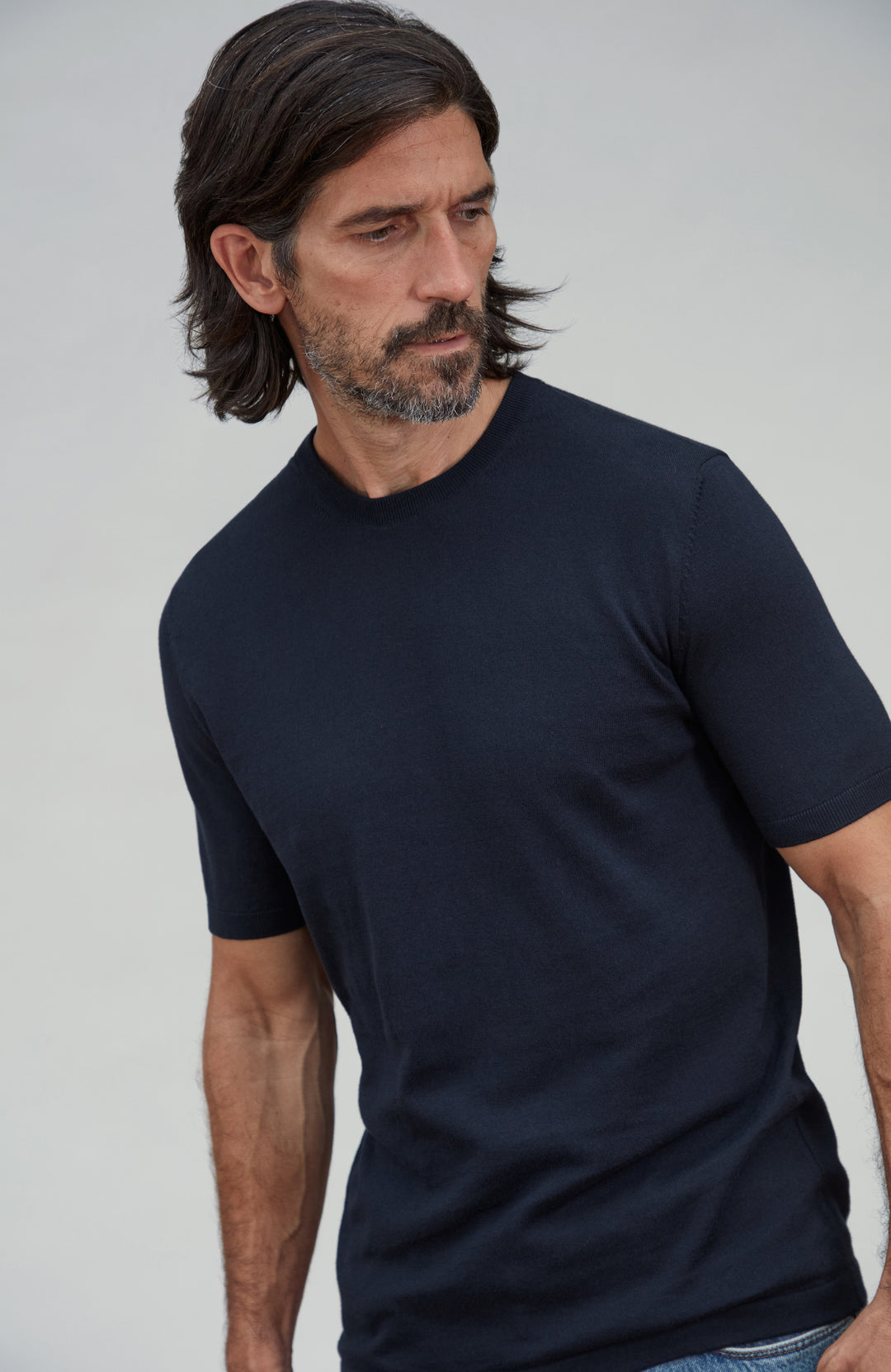A man wearing a plain dark navy cotton short-sleeve crewneck t-shirt, photographed from the chest up against a light gray studio background. By Paul James Knitwear