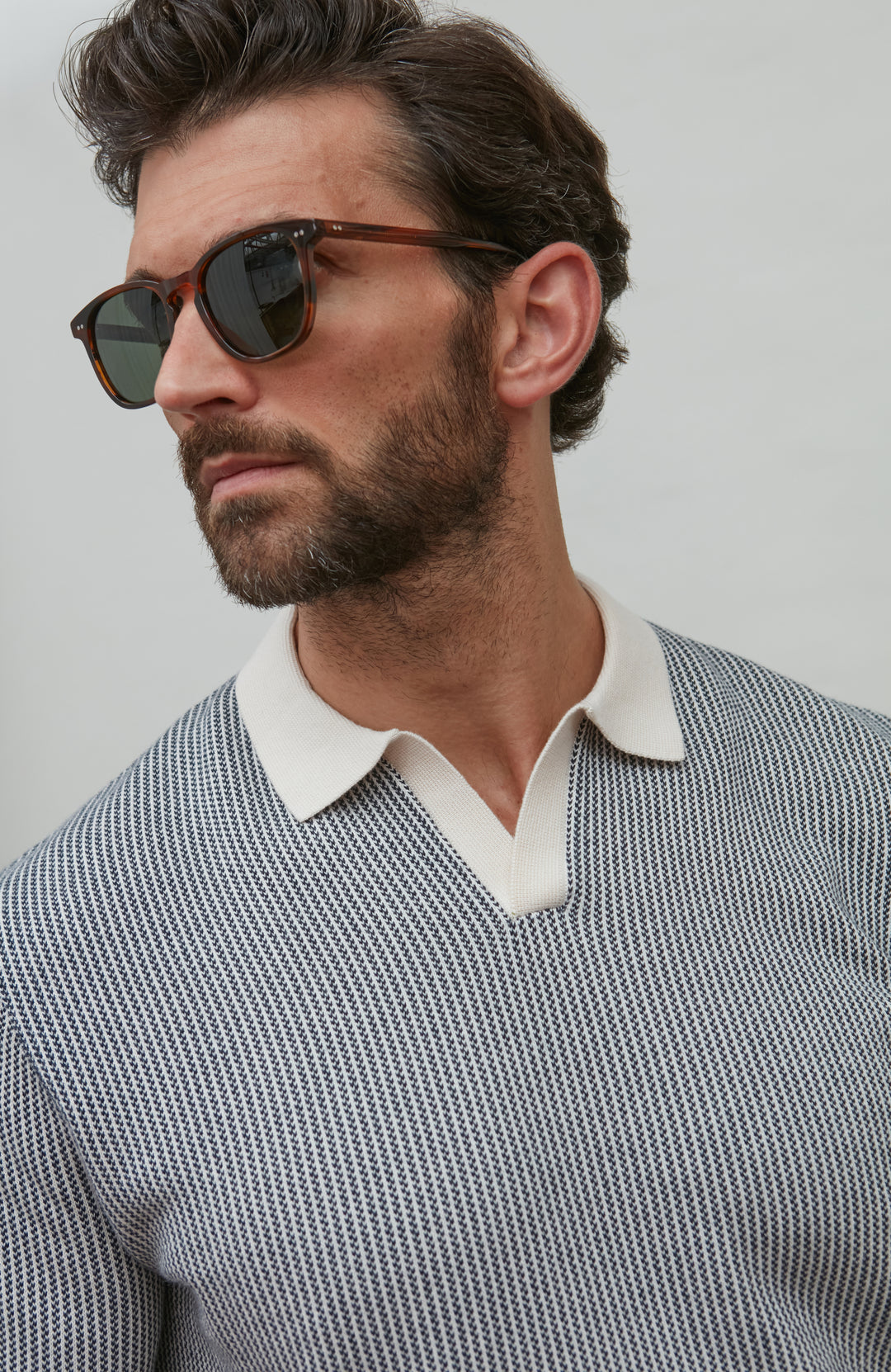 Man wearing polo shirt and sunglasses and a patterned sweater with a plain background