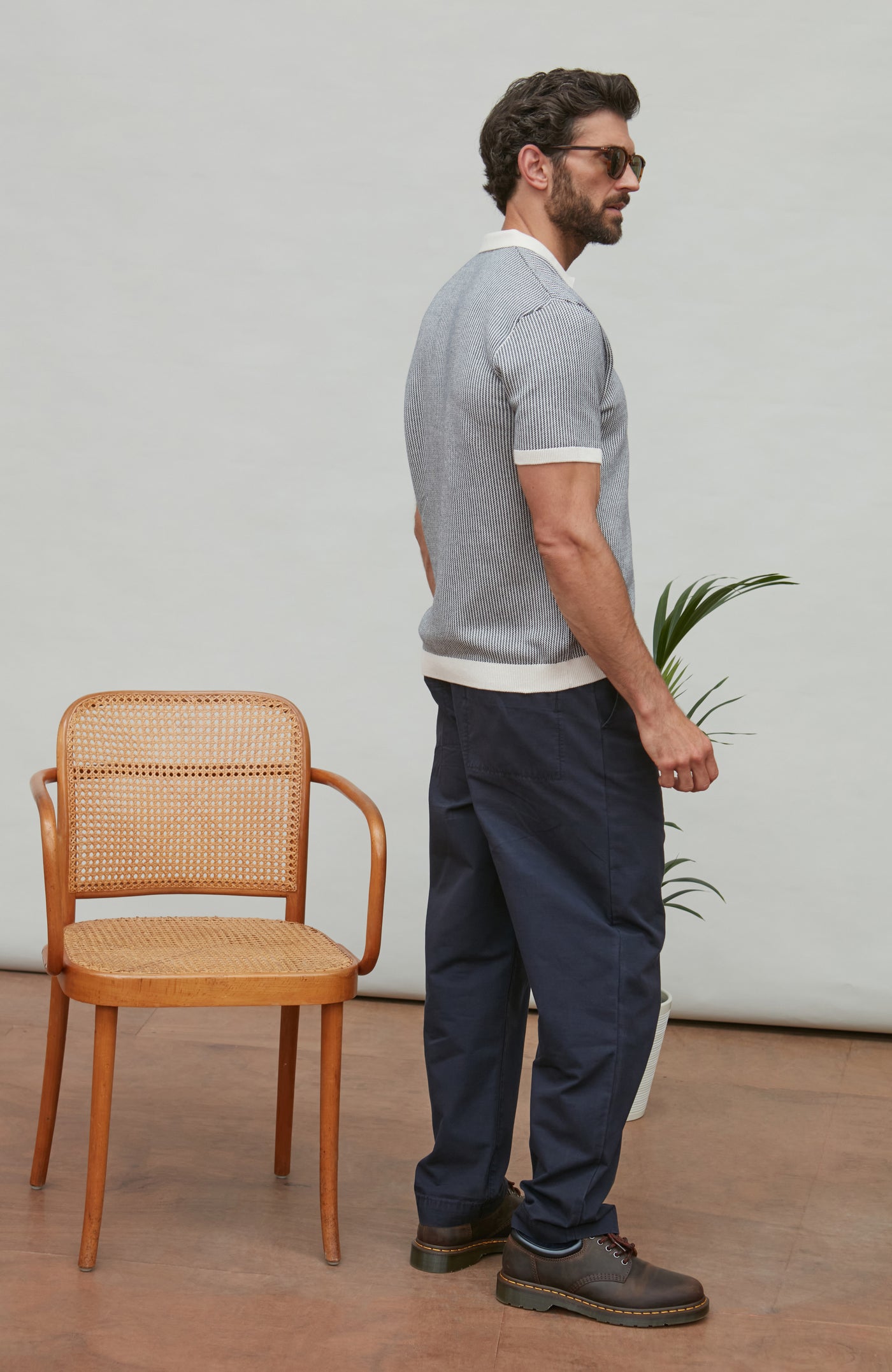 Man standing next to a wooden chair indoors with a neutral background