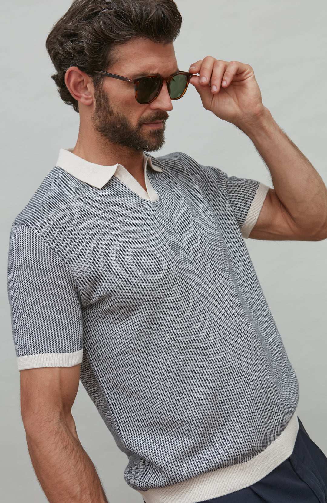Man wearing a patterned polo shirt with a white collar and sunglasses, against a plain background