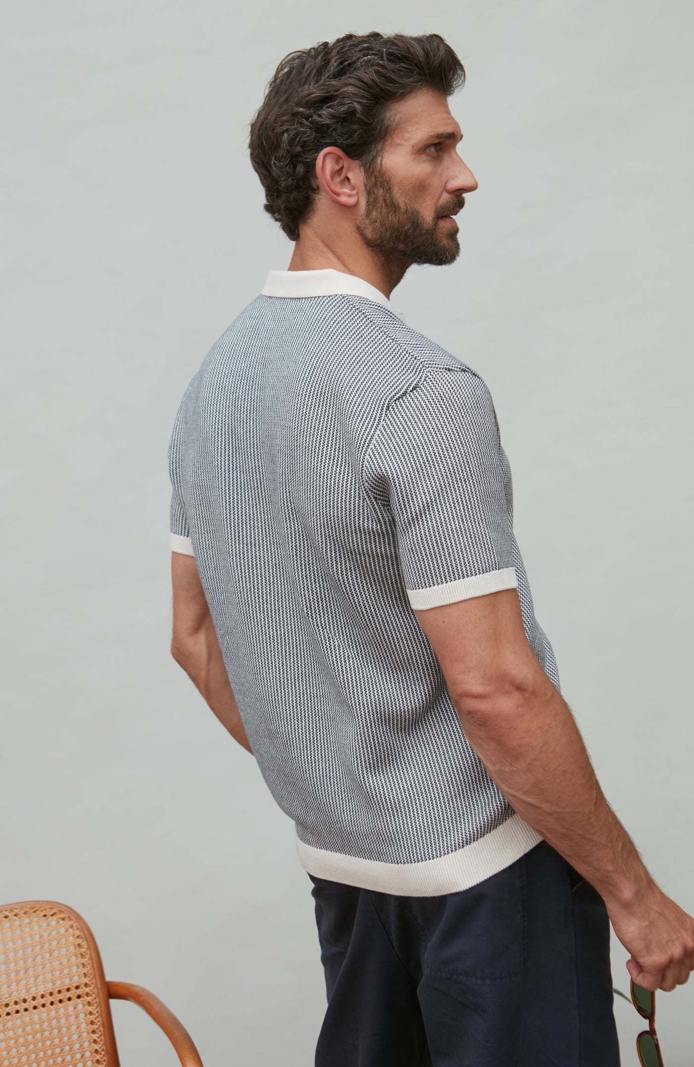 Man wearing a patterned polo shirt and dark pants against a plain background