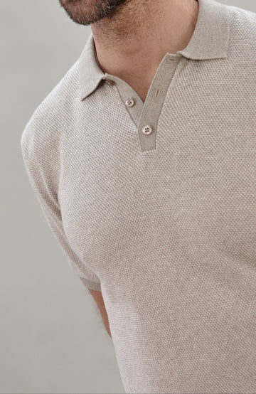Close-up of a man wearing a light beige textured short-sleeve polo shirt by Paul James Knitwear with a two-button placket.