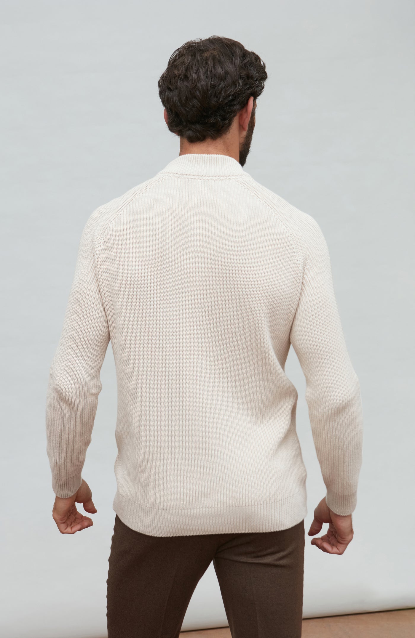 Man wearing a beige sweater and brown pants against a plain background