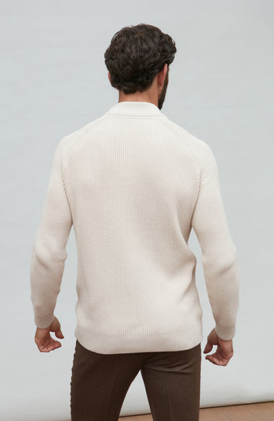 Man wearing a beige sweater and brown pants against a plain background
