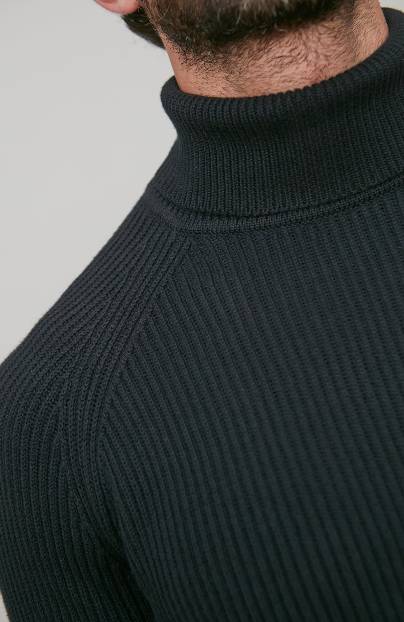 Close-up of a person wearing a black ribbed turtleneck sweater against a gray background