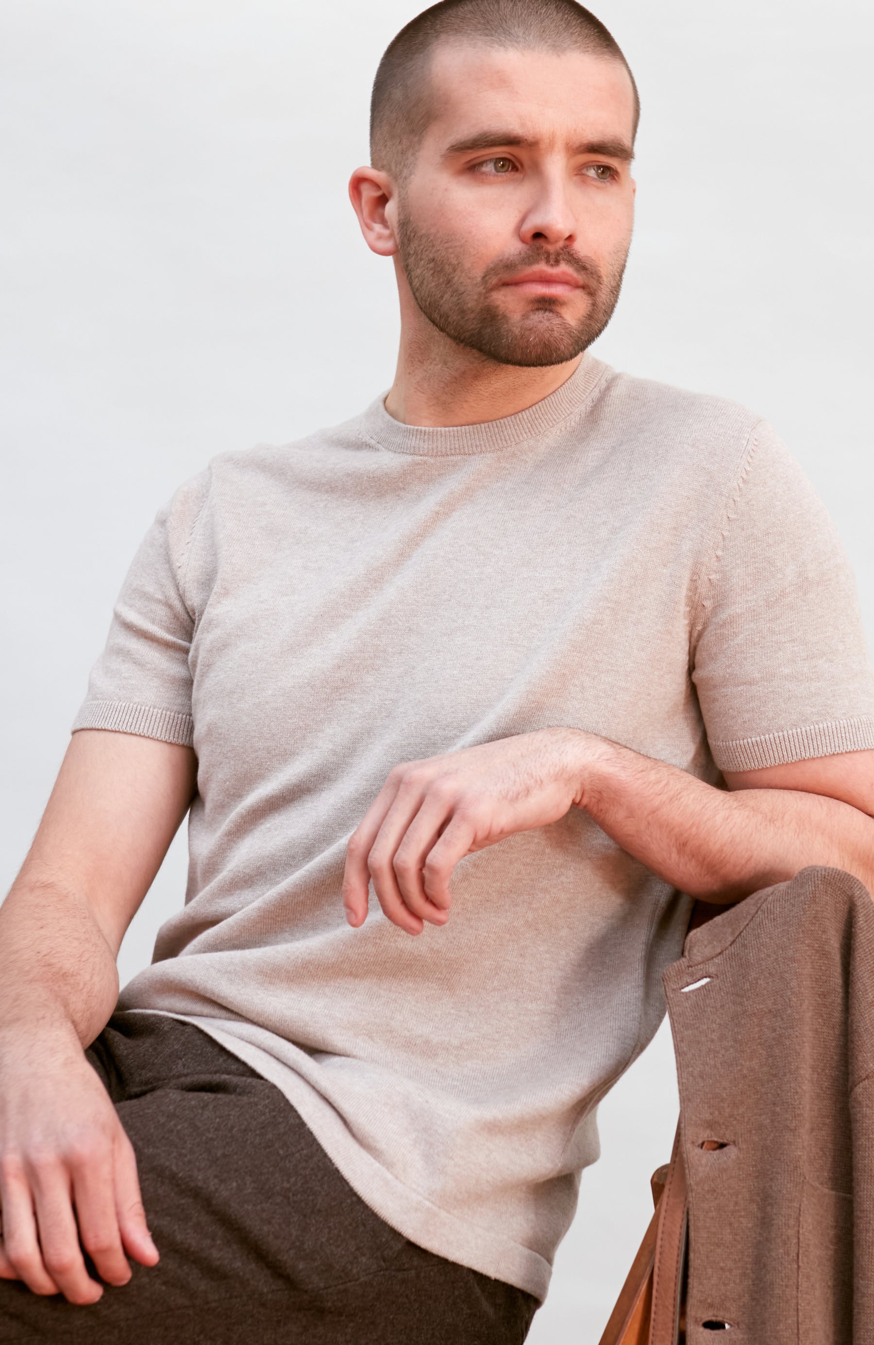 Man wearing a beige cotton t-shirt sitting on a chair by Paul James 