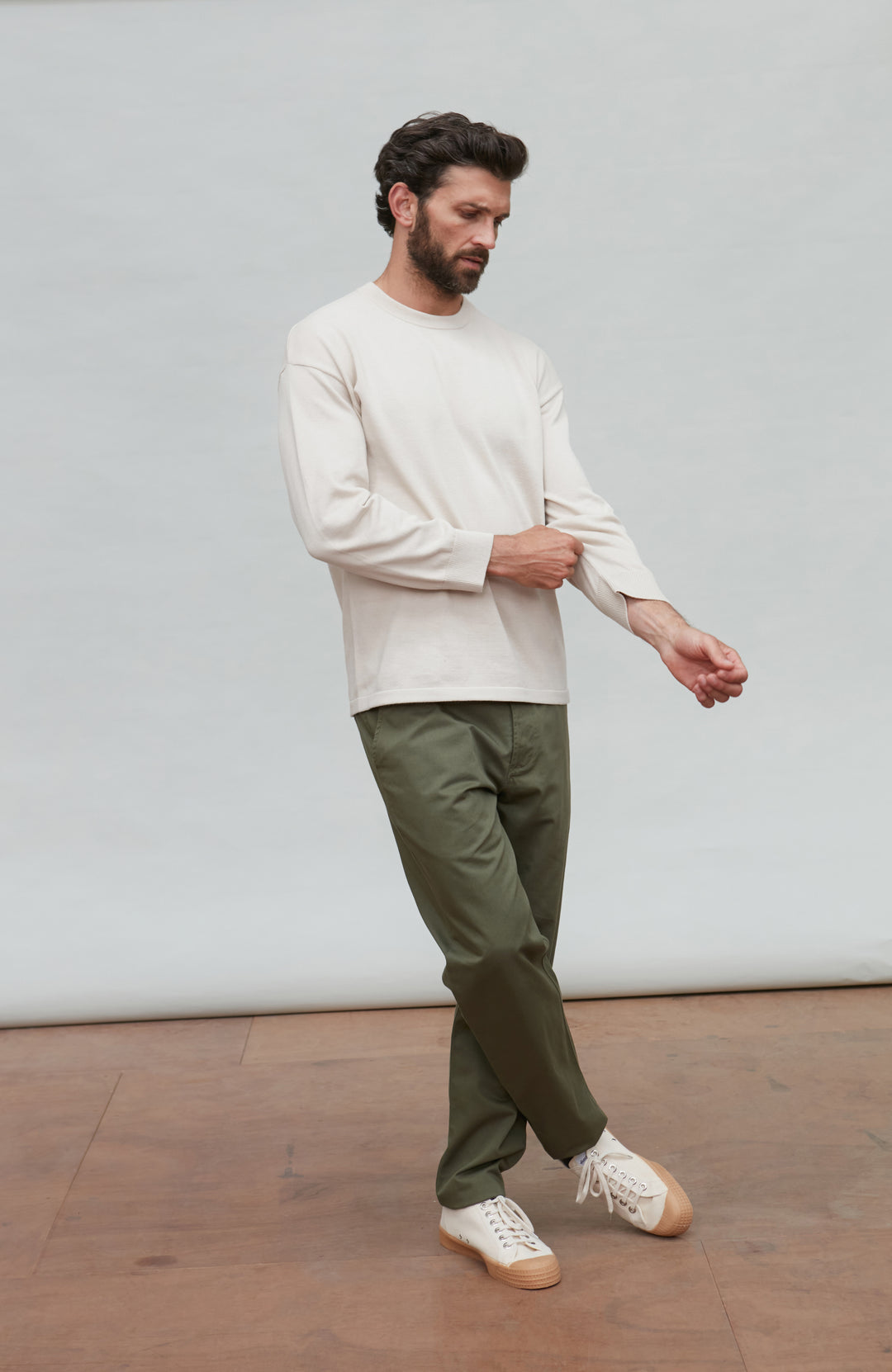 Man wearing a white cotton sweater against a plain background by Paul James