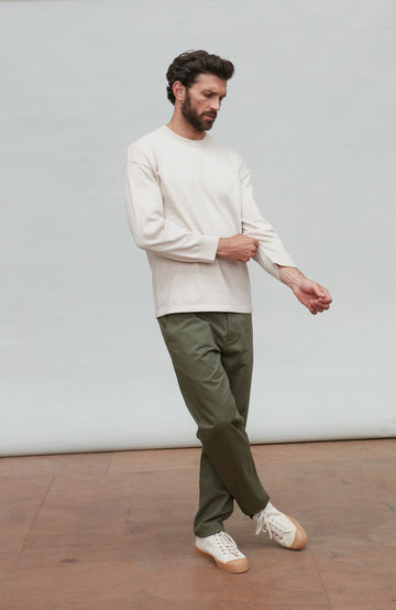 Man wearing a white cotton sweater against a plain background by Paul James