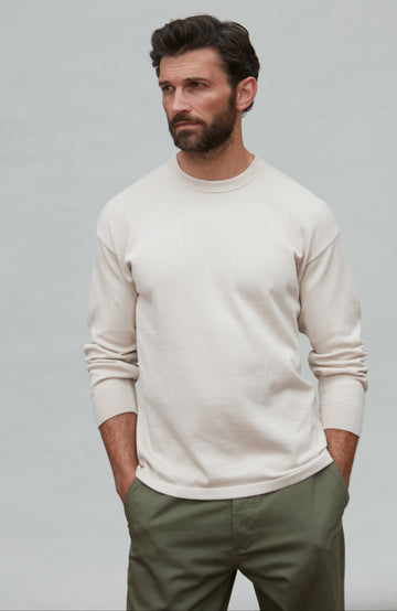 Man wearing a white cotton sweater against a plain background by Paul James
