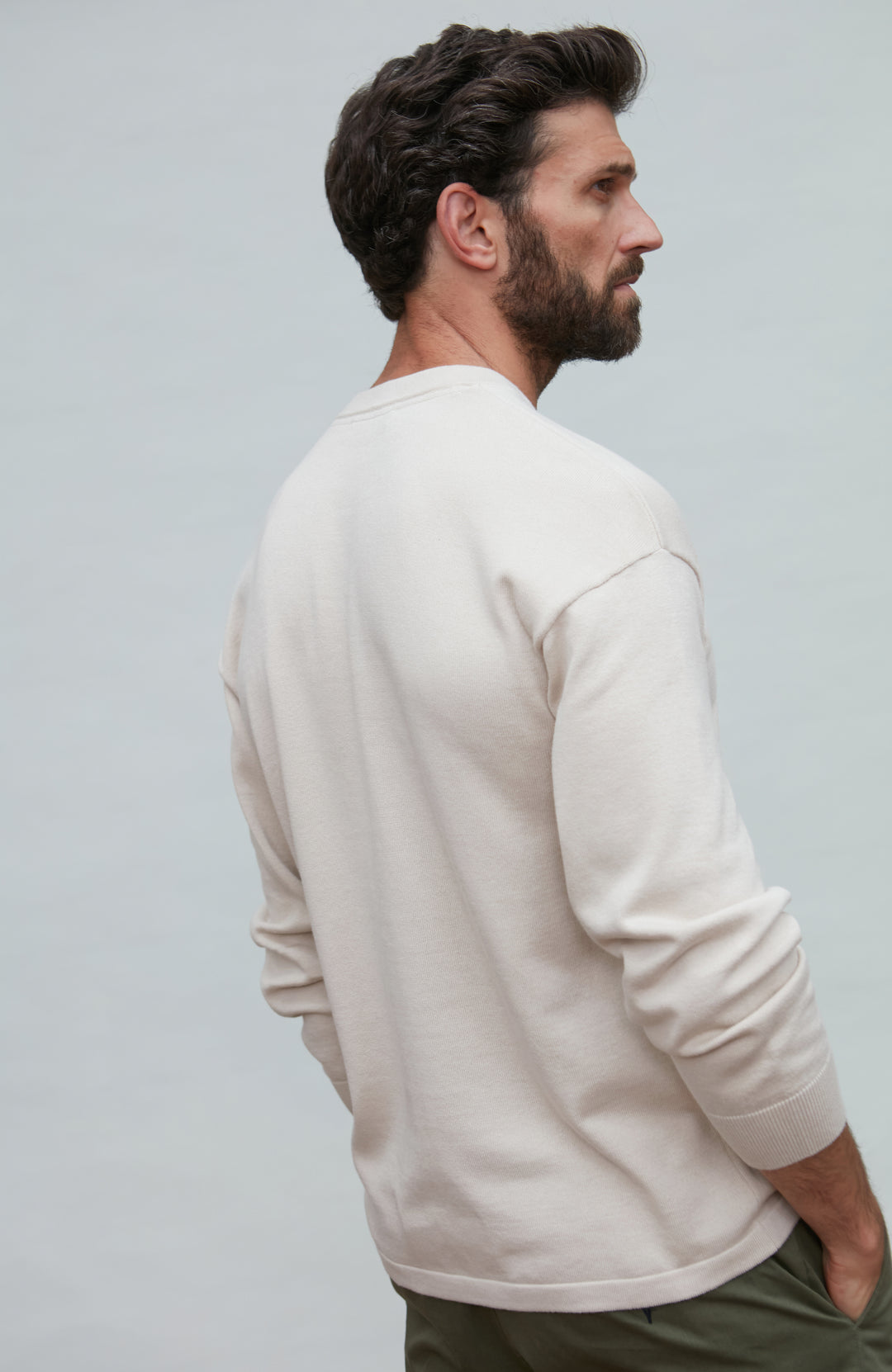 Man wearing a white cotton sweater against a plain background by Paul James