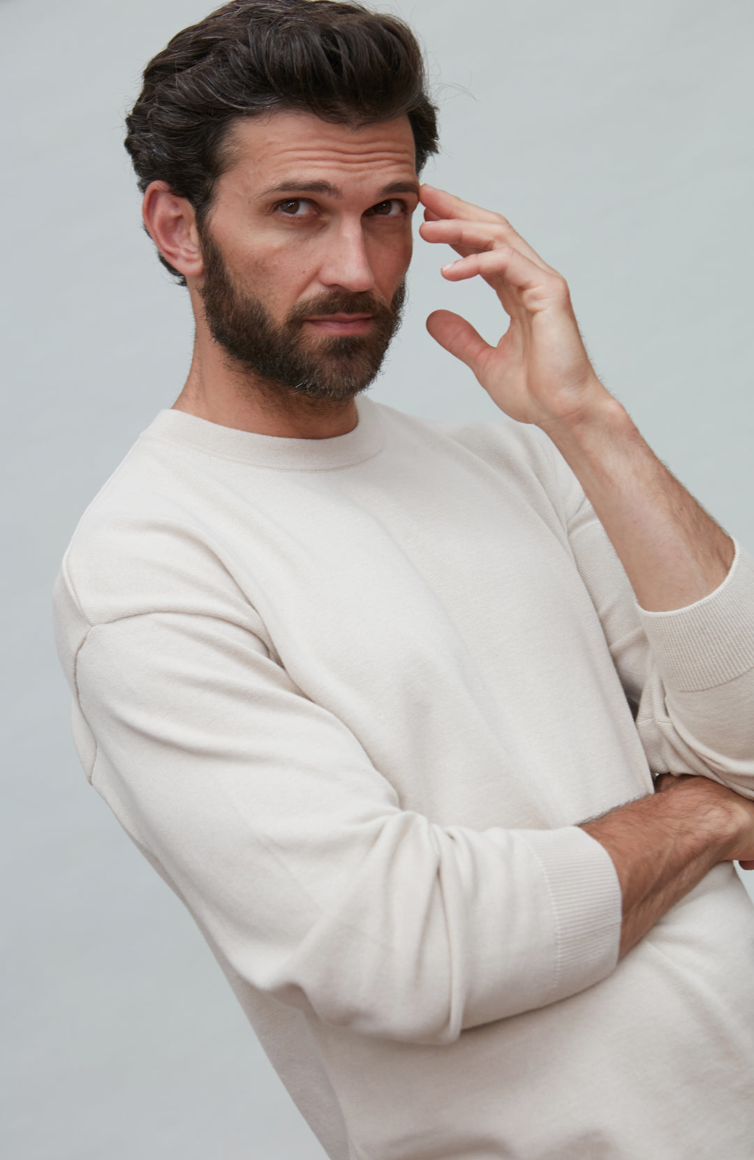 Man wearing a white cotton sweater against a plain background by Paul James