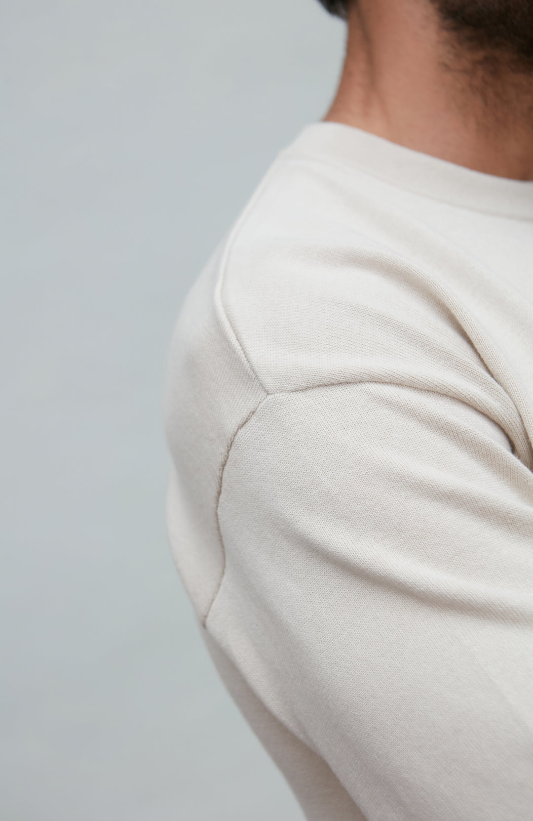 Man wearing a white cotton sweater against a plain background by Paul James