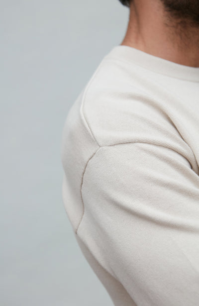 Man wearing a white cotton sweater against a plain background