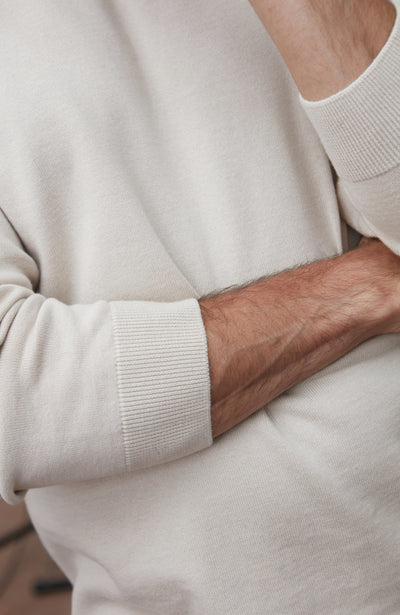 Man wearing a white cotton sweater against a plain background