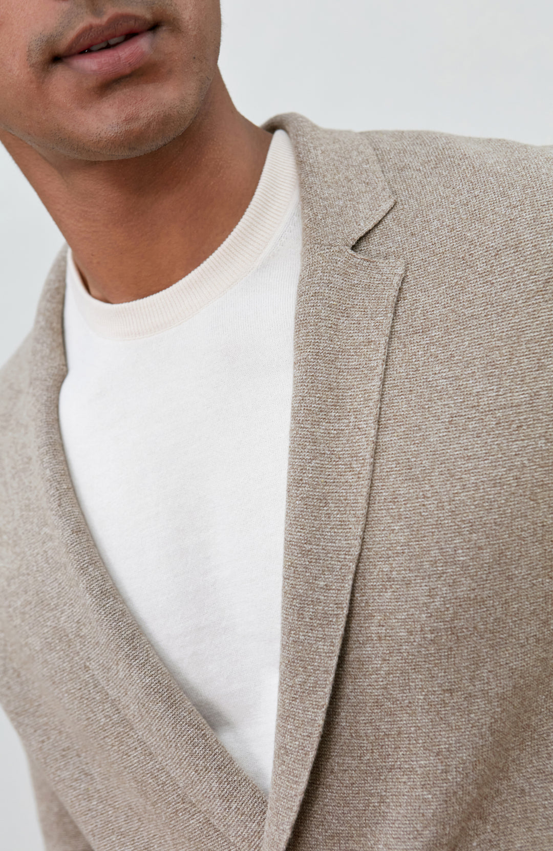 A man wearing a light beige double-breasted knit cardigan by Paul James Knitwear over a white t-shirt and brown trousers