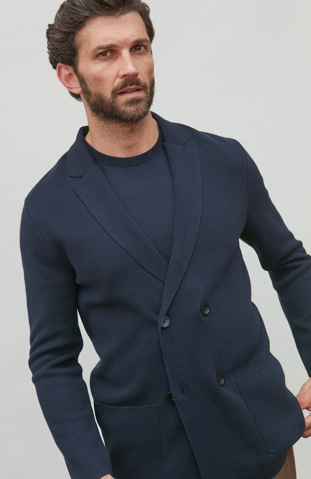 Man wearing a navy double breasted blazer over a dark shirt against a light gray background