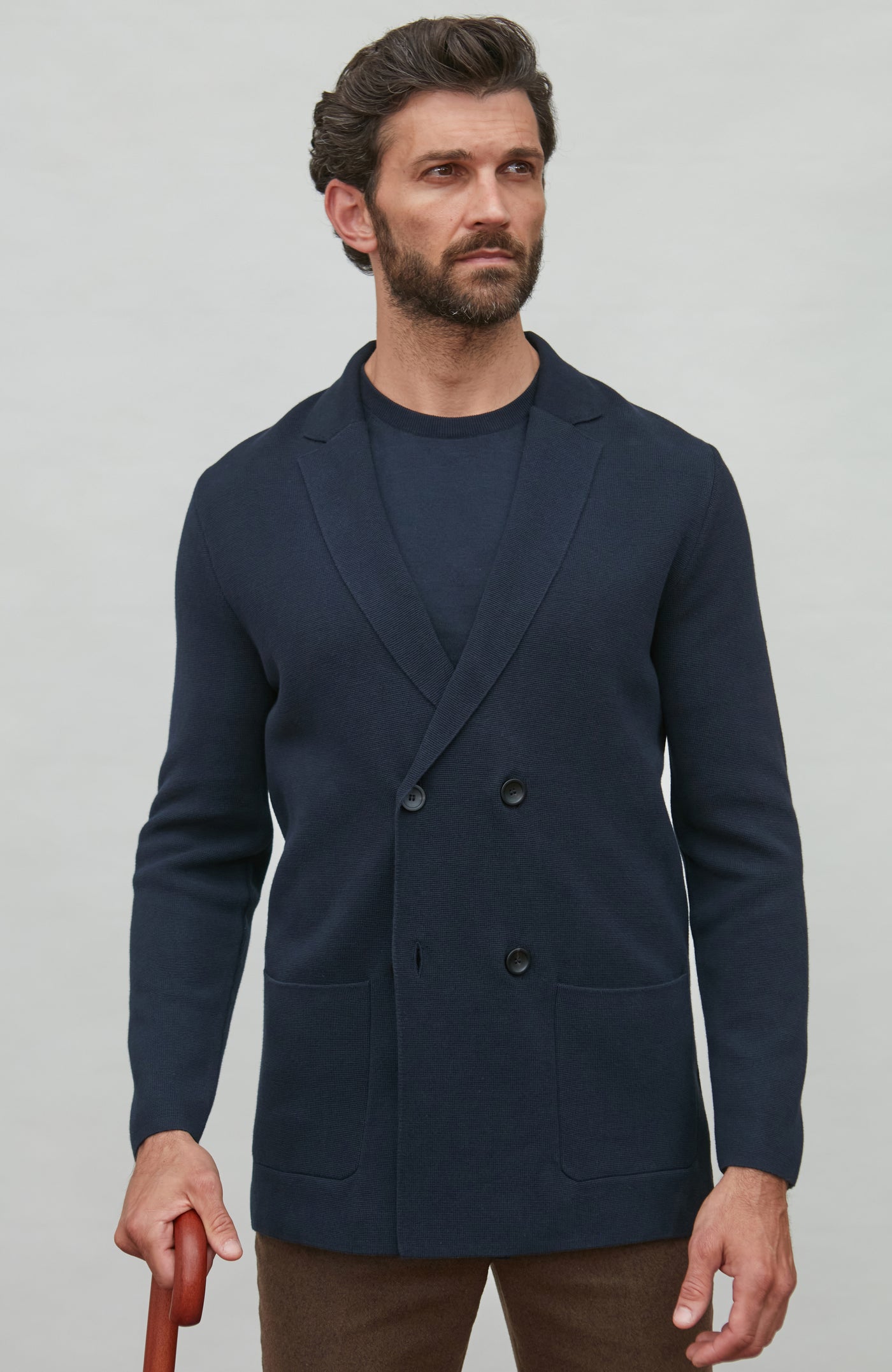 Man wearing a navy blue double breasted blazer over a dark shirt on a light gray background