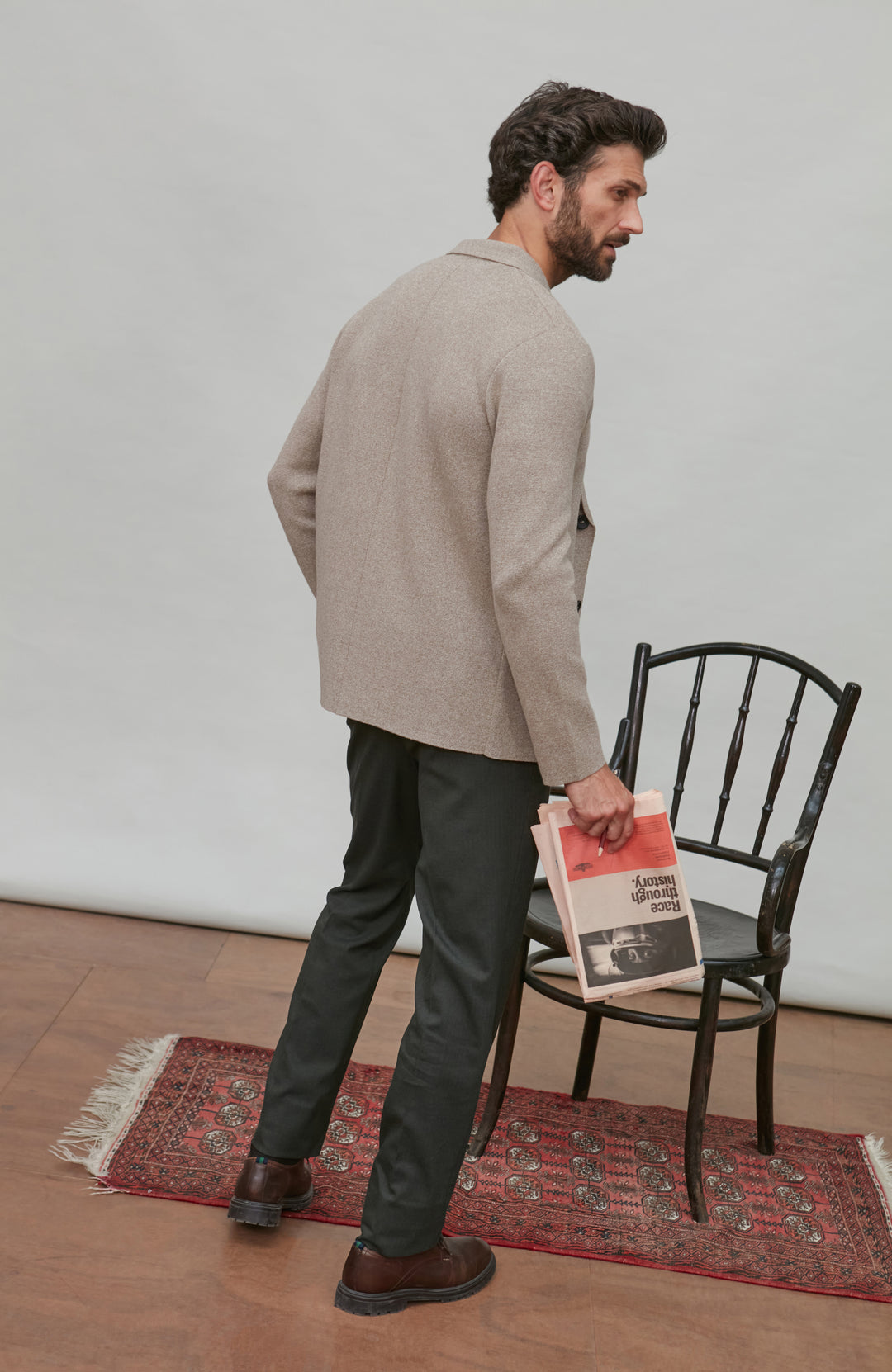 Man holding a newspaper, standing in a room with a chair and rug.