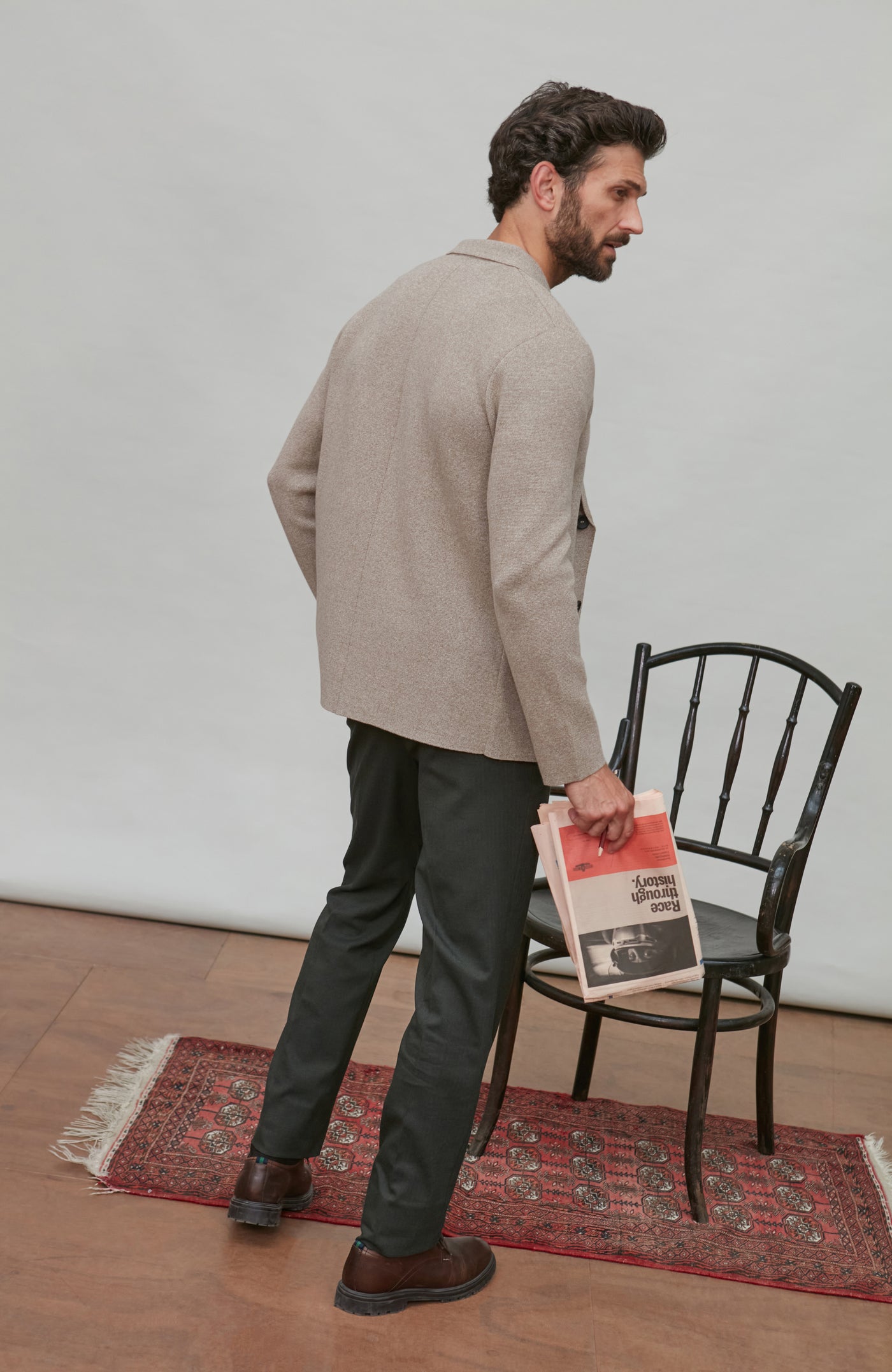 Man holding a newspaper, standing in a room with a chair and rug.