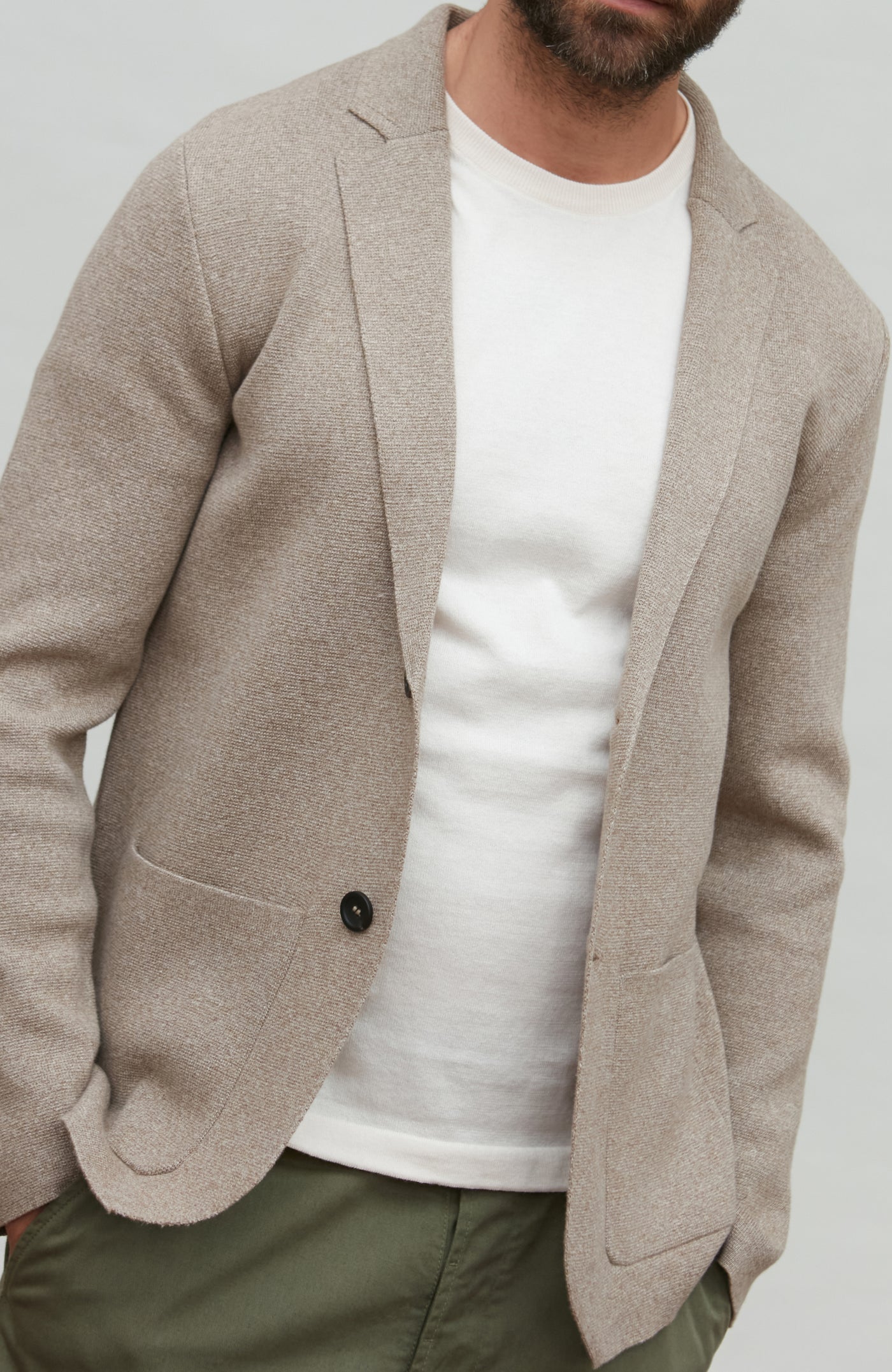 Man wearing a beige blazer over a white shirt with a plain background