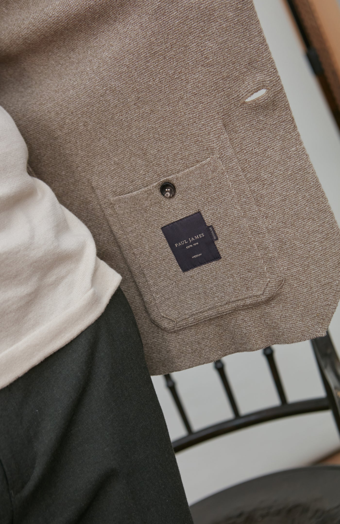 Close-up of a beige textured jacket with a paul james label on a blurred background