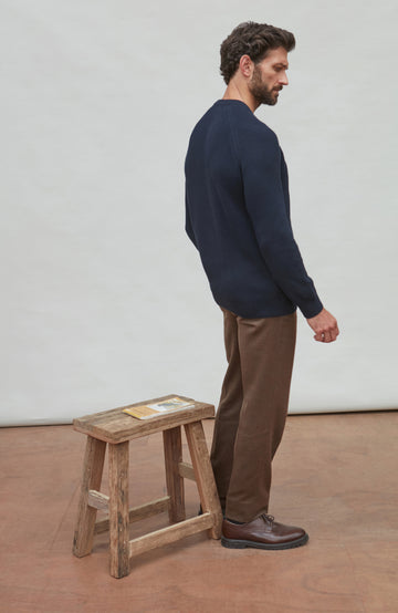 Man wearing a navy ribbed fisherman sweater and brown pants against a plain background